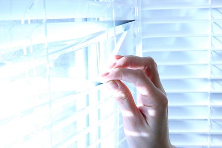 Someone looking out of window opening blinds