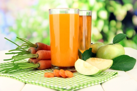 Glasses of juice, apples and carrots on white wooden table, on green backgroundの写真素材