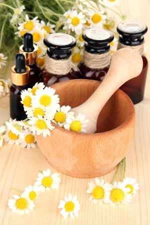 Essential oil and chamomile flowers in mortar on wooden tableの写真素材