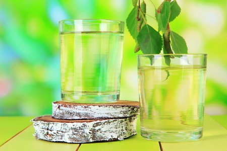 Glasses of birch sap on wooden table, on green backgroundの写真素材