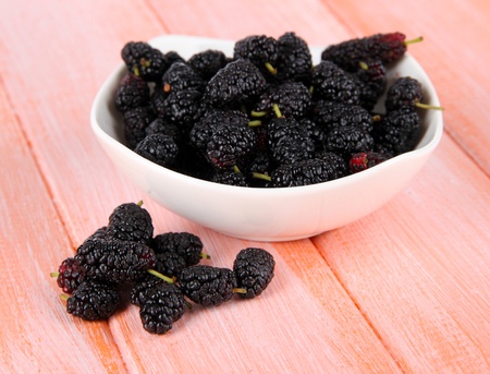 Ripe mulberries in bowl on wooden background