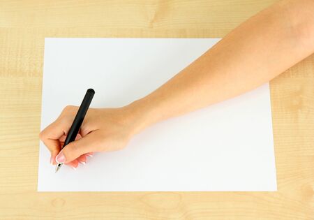 Hand with pen on white paper, on wooden backgroundの写真素材