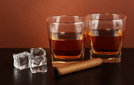Glasses of whiskey and cigar on brown backgroundの写真素材