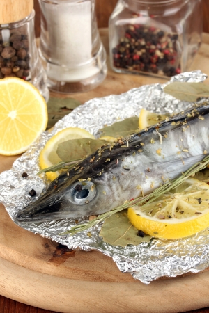 Fish in foil with herbs and lemon on board on wooden table close-upの写真素材