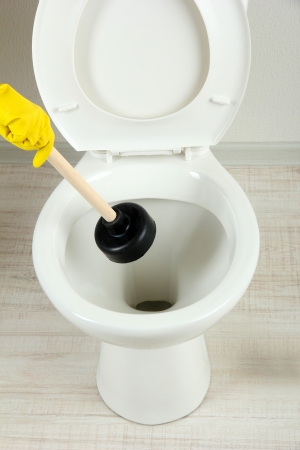 Woman uses a plunger to unclog a toilet bowl in a bathroomの写真素材