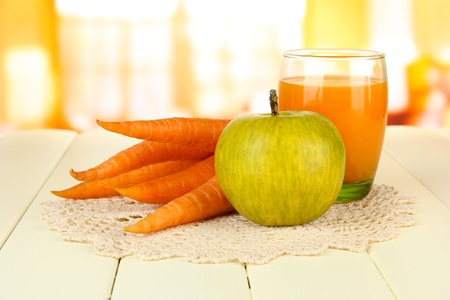 Heap of carrots and green apple, glass of juice, on color wooden  table on bright backgroundの写真素材