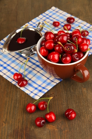 Ripe red cherry berries in cup and chocolate sauce on wooden table close-upの写真素材