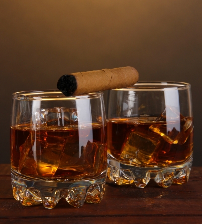 Brandy glasses with ice and cigar on wooden table on brown backgroundの写真素材