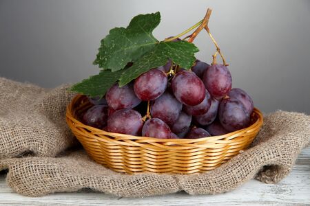 Ripe delicious grapes in wicker basket on table on gray background