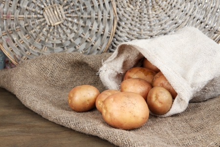 Potato in sack on sackcloth, on wooden table on wicker tray backgroundの写真素材