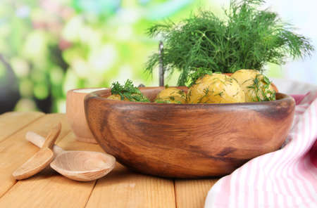 Boiled potatoes on wooden bowl near napkin on wooden table on nature backgroundの写真素材