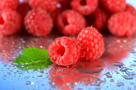 Ripe sweet raspberries with drops, on blue background