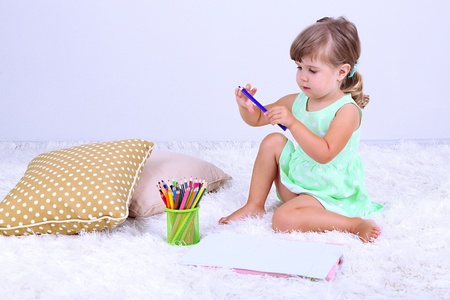 Little cute girl sitting on carpet and drawing pictures, on gray backgroundの写真素材