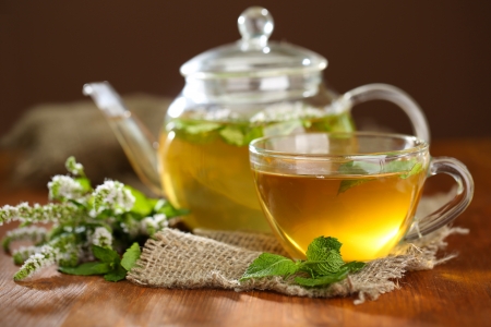 Cup and teapot of herbal tea with fresh mint flowers on wooden tableの写真素材