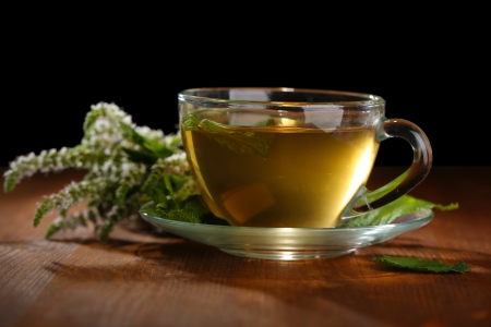 Cup of herbal tea with fresh mint flowers on wooden table on black backgroundの写真素材