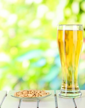 Beer in glass and nuts on table on nature backgroundの写真素材