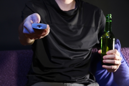 Man hand holding a TV remote control and beer bottle, on dark backgroundの写真素材