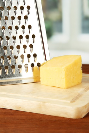 Metal grater and cheese on cutting board, on bright backgroundの写真素材