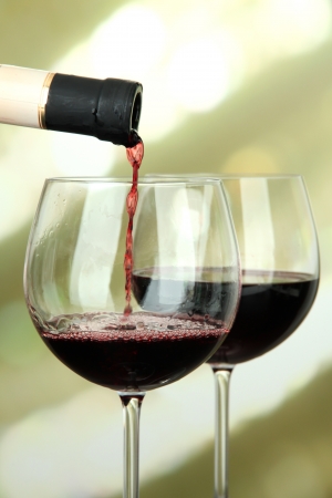 Red wine being poured into wine glass, on bright backgroundの写真素材