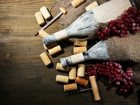 Old bottles of wine, grapes and corks on wooden background