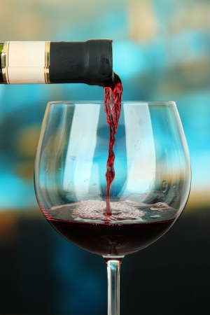 Red wine being poured into wine glass, on bright backgroundの写真素材