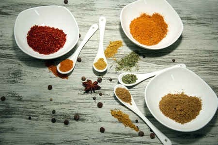 Assortment of spices in  white spoons and bowls, on wooden background