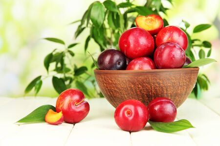 Ripe plums in bowl on wooden table on natural backgroundの写真素材