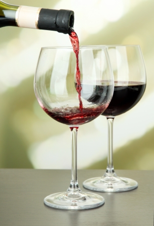 Red wine being poured into wine glass, on bright backgroundの写真素材