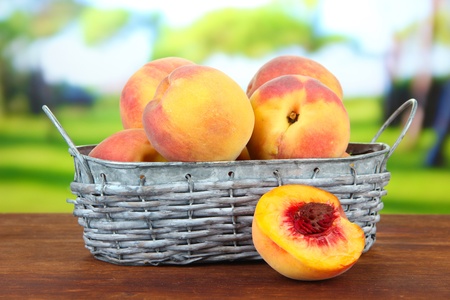 Ripe sweet peaches in wicker basket, on bright backgroundの写真素材