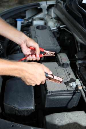 Car mechanic uses battery jumper cables to charge dead batteryの写真素材