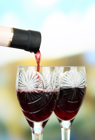 Red wine being poured into wine glass, on bright backgroundの写真素材