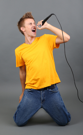 Handsome young man sings on grey backgroundの写真素材