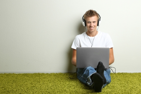 Young man relaxing on carpet and listening to music, on gray wall backgroundの写真素材