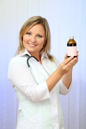Young beautiful doctor  holding bottle of medicament, on light backgroundの写真素材