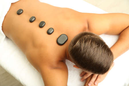 Young man relaxing with hot stones on back before massage