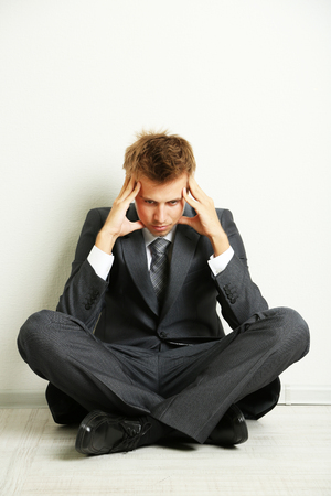 Young businessman  sitting on floor, on gray wall backgroundの写真素材