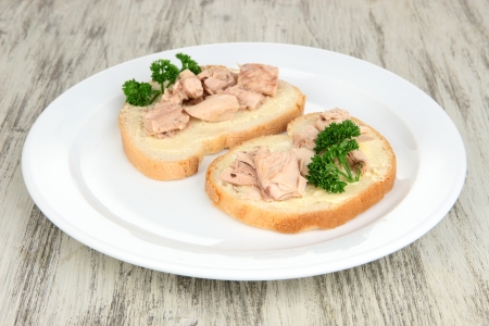 Tasty sandwiches with tuna and cod liver sardines, on white plate. on wooden backgroundの写真素材