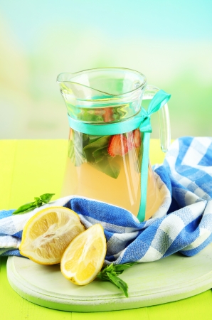 Basil lemonade with strawberry in  jug and glass, on wooden table, on bright backgroundの写真素材