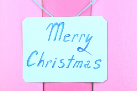 Signboard with words Merry Christmas on pink wooden table background close-upの写真素材