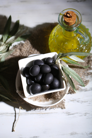 Olive oil and olives in bowl on sackcloth on wooden tableの写真素材
