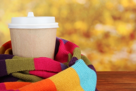 Hot drink in paper cup with color scarf on wooden table bright backgroundの写真素材