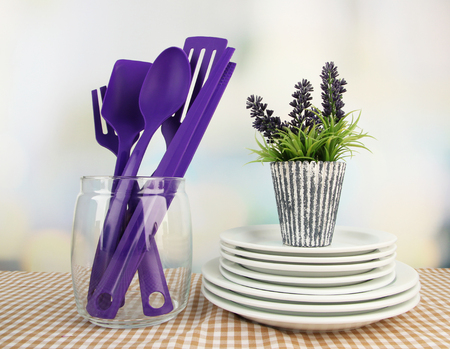 Plastic kitchen utensils in stand with clean dishes on tablecloth on bright の写真素材