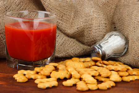 Delicious crackers with salt and tomato juice on wooden table on sackcloth backgroundの写真素材