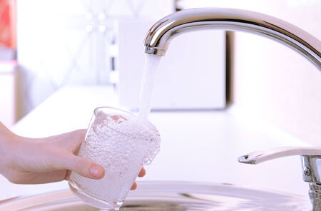 Hand holding  glass of water poured from  kitchen faucet