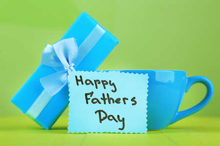 Happy Fathers Day tag with gift box and cup, on wooden table, on light の写真素材