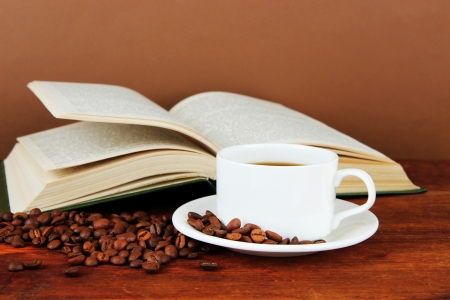 Cup of coffee with coffee beans and book on wooden table on brown backgroundの写真素材