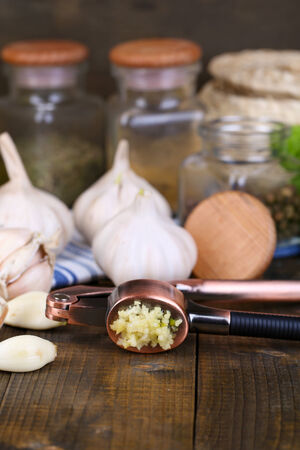 Composition with garlic press, fresh garlic and glass jars with spices on wooden backgroundの写真素材