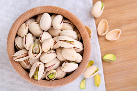 Pistachio nuts in wooden bowl on fabric backgroundの写真素材
