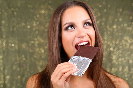 Portrait of beautiful young girl with chocolate on shiny background