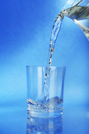 Pour water from  pitcher into  glass, on dark blue の写真素材